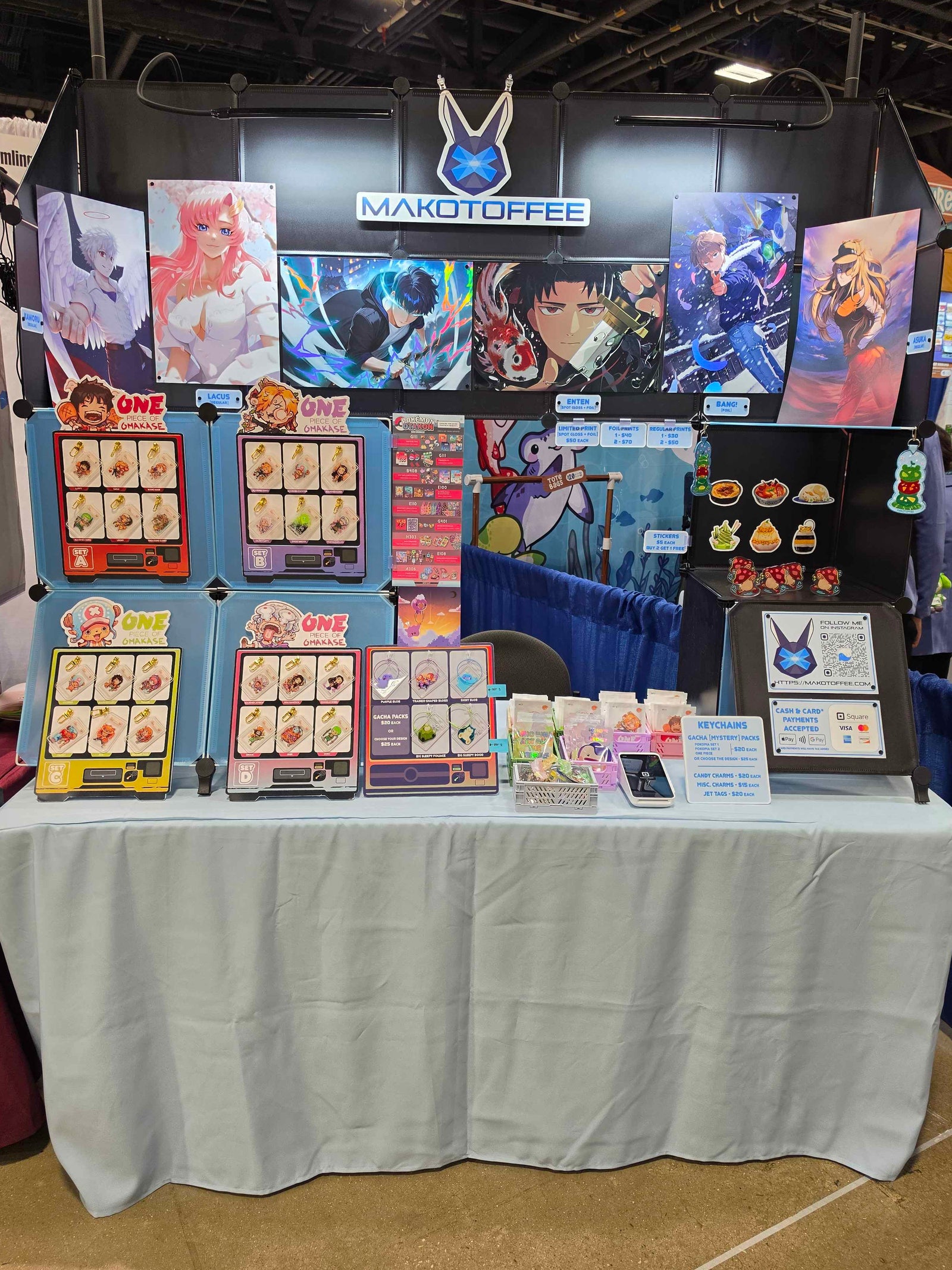 A booth display for makotoffee at Otakon 2026, featuring anime-inspired prints, keychains, stickers, and standees.
